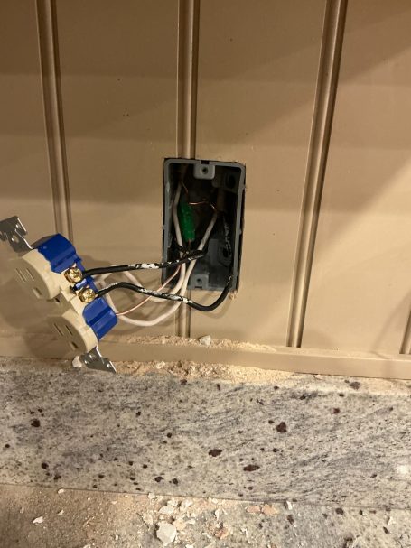 Electrical outlet box with wires and a blue electrical connector against a wall.