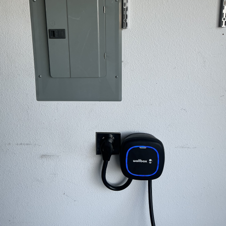 Electric vehicle charger mounted on a wall next to a gray electrical panel.