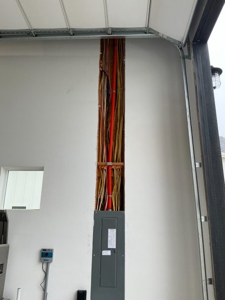 Electrical panel with exposed wires running along a wall in a garage.