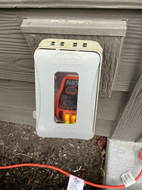 A wall-mounted electrical outlet tester displaying red and yellow lights.